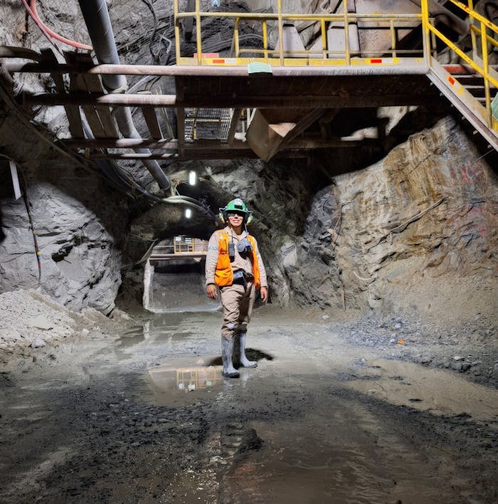 Engineer standing in an illuminated underground mine tunnel, showcasing mining safety gear and modern infrastructure.