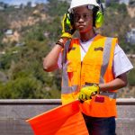 Woman in safety gear with a traffic cone, outdoors on a sunny day.